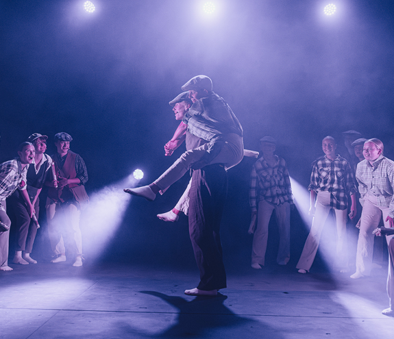 Ungdommer på en scene, der en gutt bærer en annen på ryggen mens flere står rundt dem.