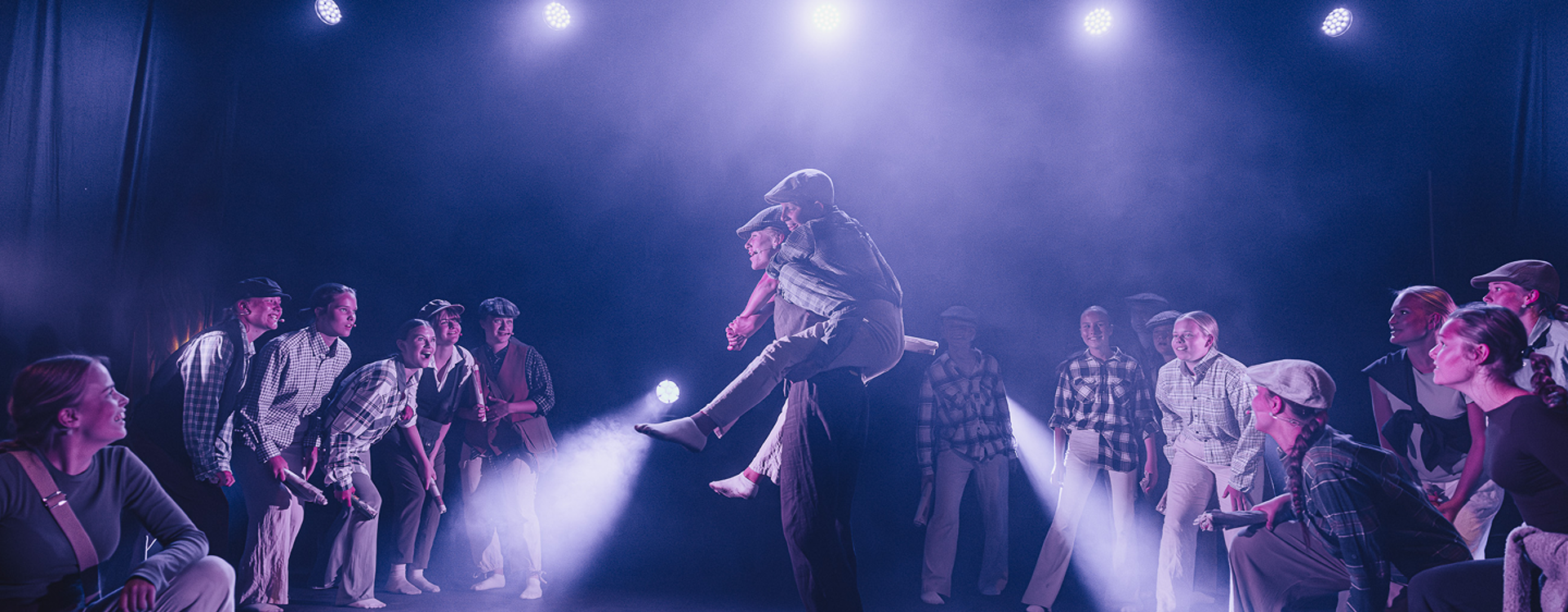 Ungdommer på en scene, der en gutt bærer en annen på ryggen mens flere står rundt dem.