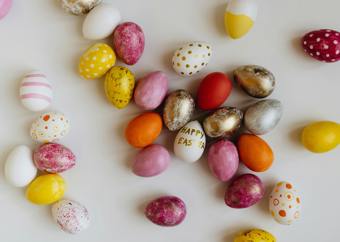 Flere fargerike påskeegg ligger strødd utover en hvit bakgrunn. På ett av dem står det "Happy easter".