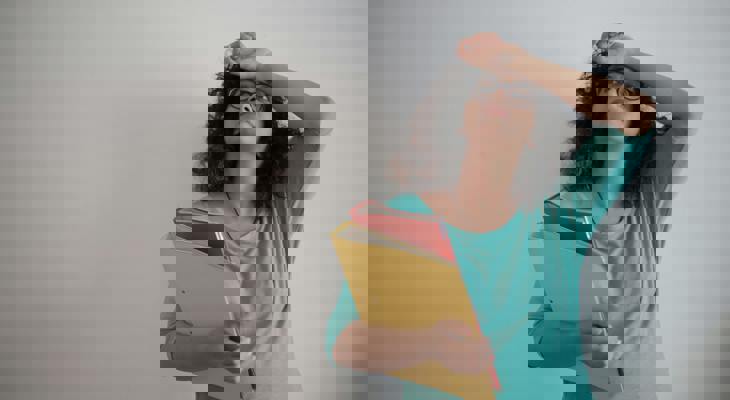 Dame med to permer i hånden og hånden mot pannen, som om hun tenker.