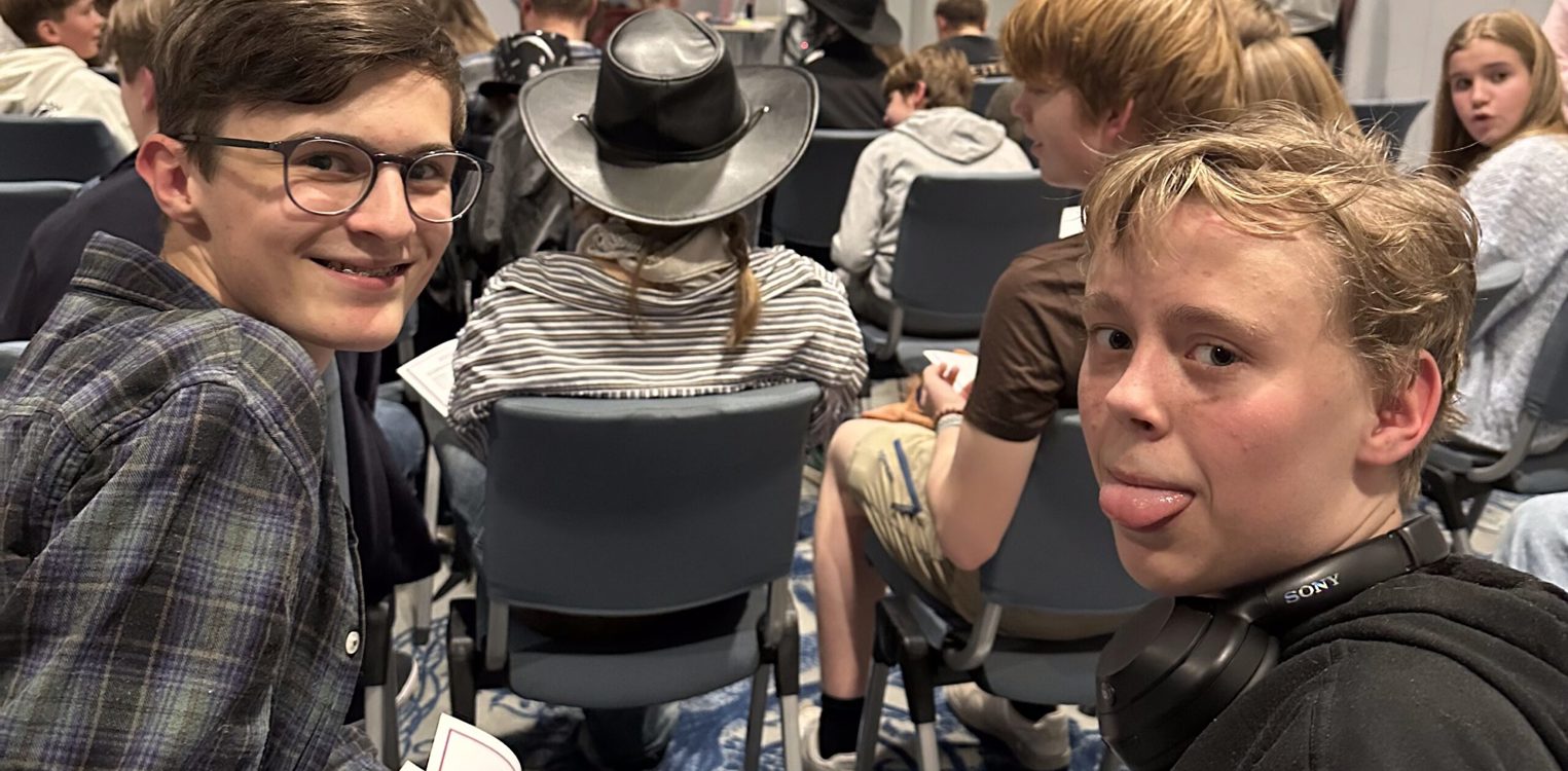 Ungdommer sitter på stoler og ser fremover; to gutter bakerst ser mot kamera, én smiler og den andre gjeiper.