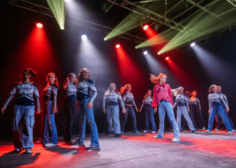 Ungdommer danser på en scene med grønt og rødt lys, kledd i hvite og blå sportsantrekk med teksten «Angels» på brystet.