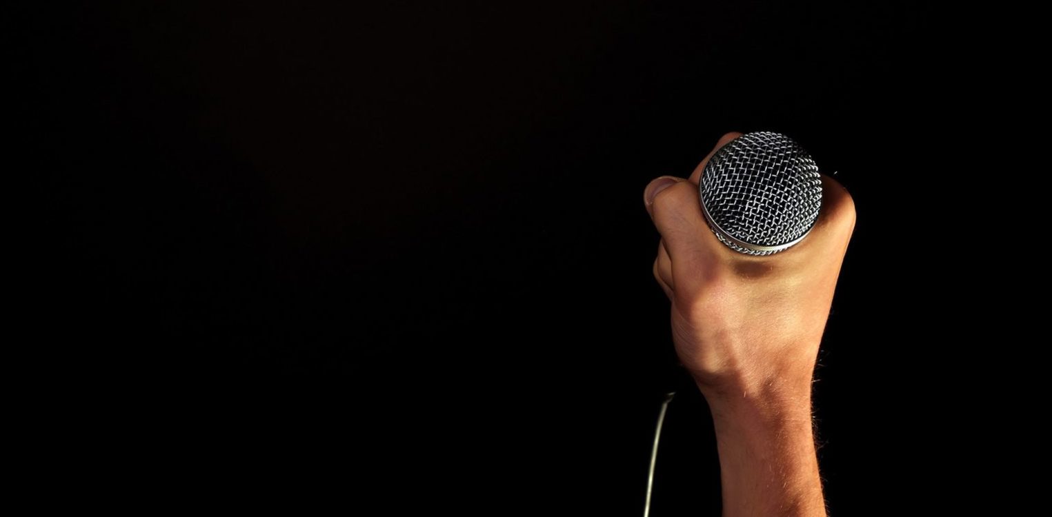 Hånd som holder en mikrofon med ledning mot en helt sort bakgrunn.