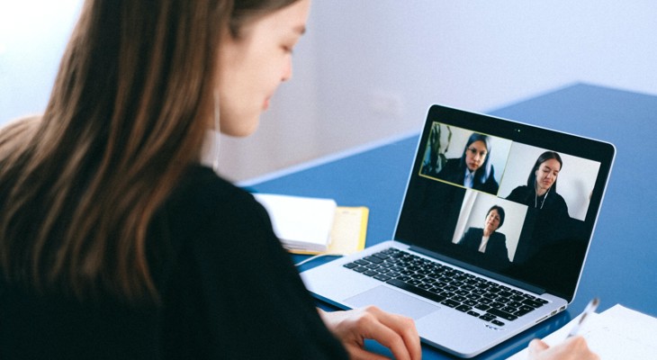 Kvinne deltar i webinar på laptop og holder en kulepenn i hånden med notatark ved siden.