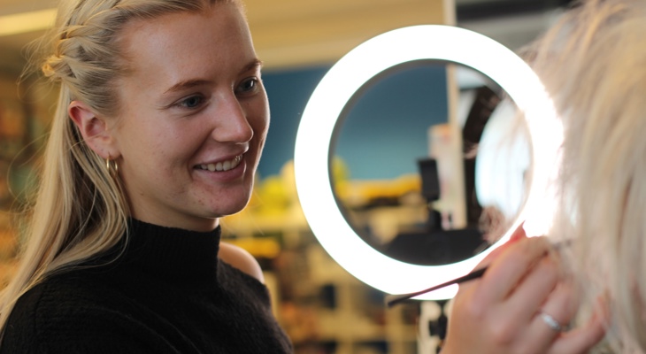 Nathalie fra Frilynt sminker en annen dame med pensel, med ringlys i bakgrunnen.