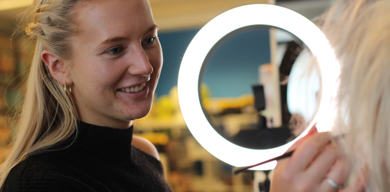 Nathalie fra Frilynt sminker en annen dame med pensel, med ringlys i bakgrunnen.