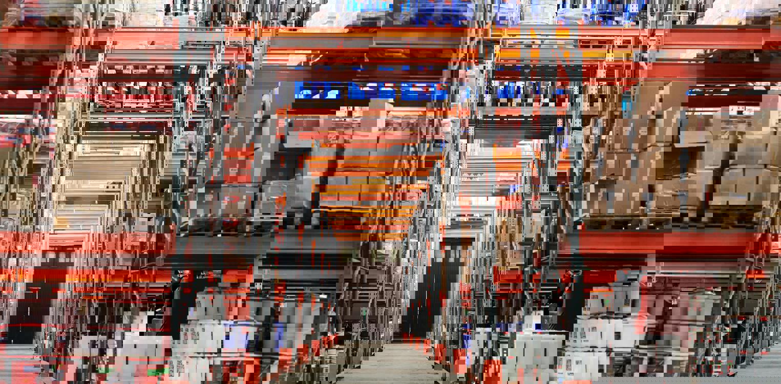 Lagergang med reoler på begge sider fylt med pappesker. Bilde av Tiger Lily: https://www.pexels.com/nb-no/bilde/industri-fabrikk-lager-virksomhet-4483610/