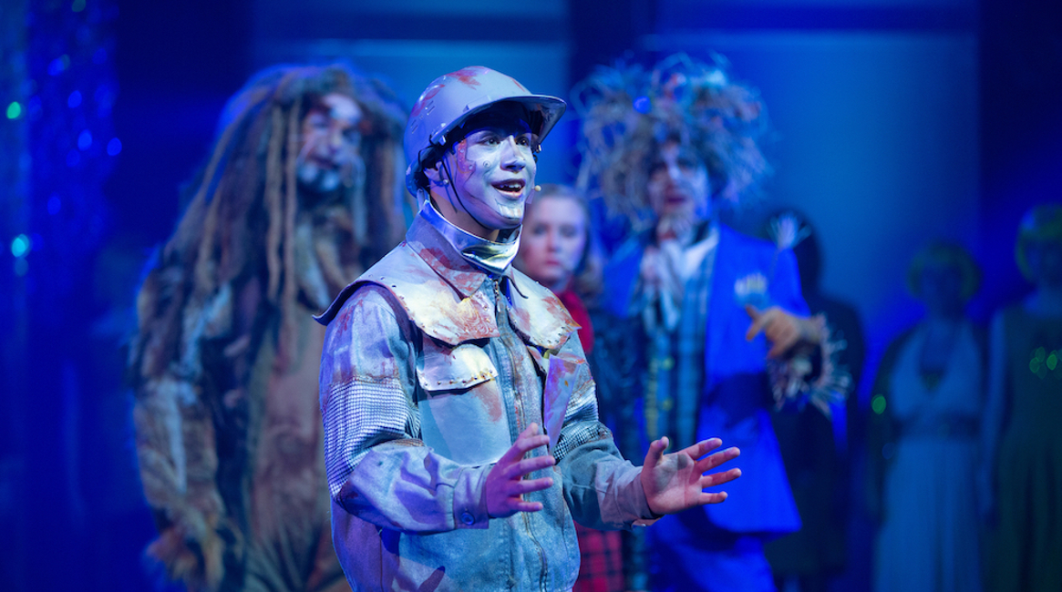 Blikkmannen fra Trollmannen fra Oz synger, med de andre karakterene stående i bakgrunnen.