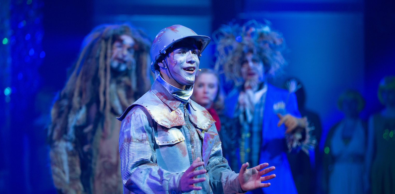 Blikkmannen fra Trollmannen fra Oz synger, med de andre karakterene stående i bakgrunnen.